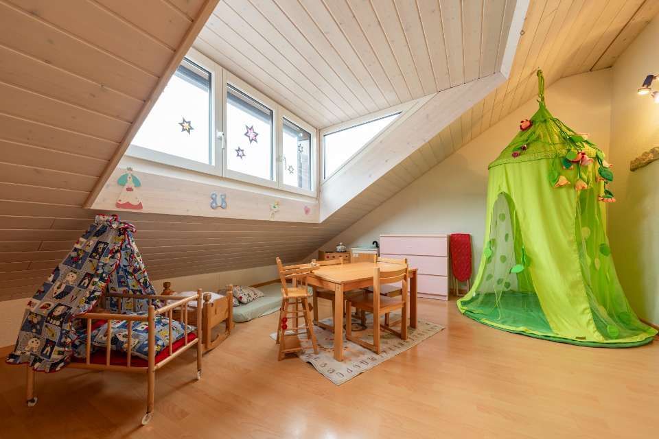 Spielzimmer im Dachgeschoss mit Dachschräge, Fenstern, kleinem Tisch, Bett und Spielzelt.