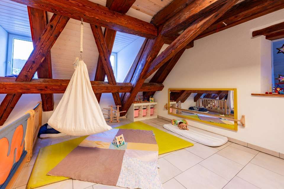 Spielzimmer mit Holzbalken, Schaukel, gelber Matte und Spiegel.