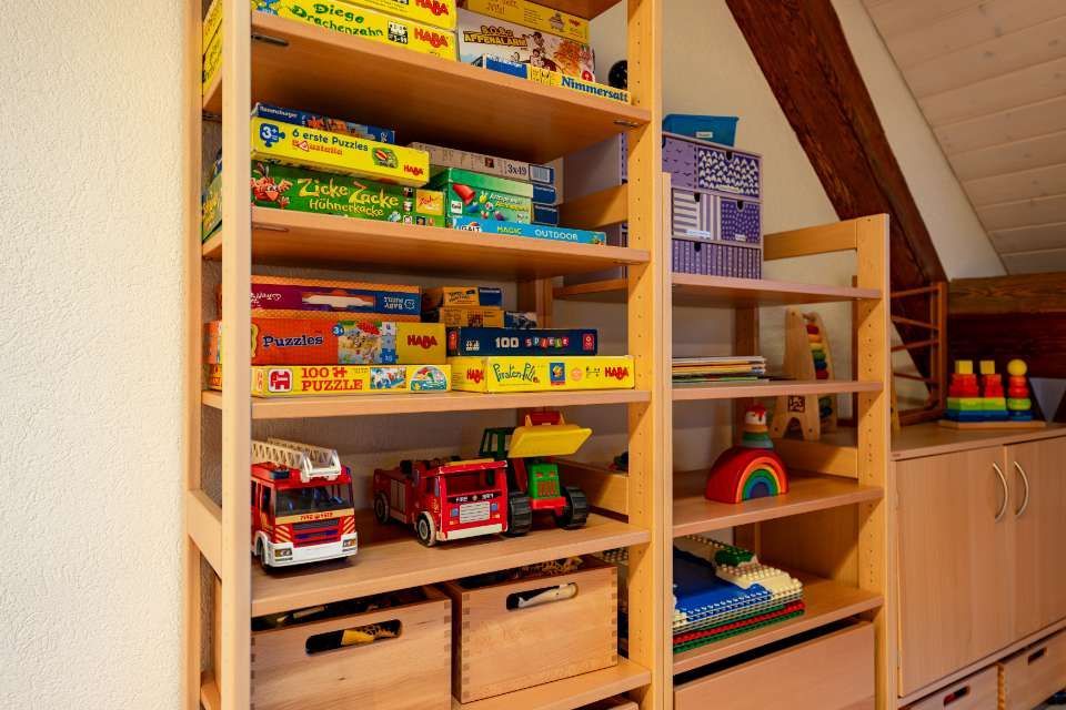 In einem Zimmer mit Dachschräge stehen Holzregale voller Spielzeug, Spiele und Aufbewahrungsboxen.