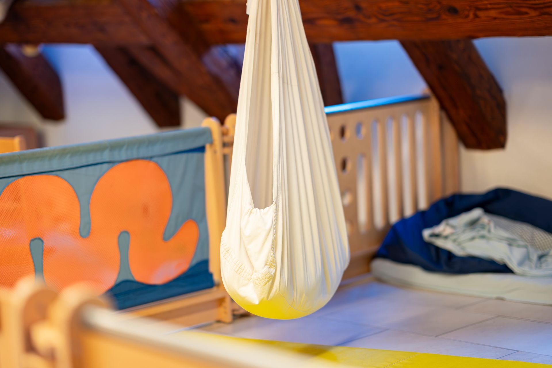 Weiße Babyhängematte, die an einem Holzbalken über einem Kinderbett befestigt ist.