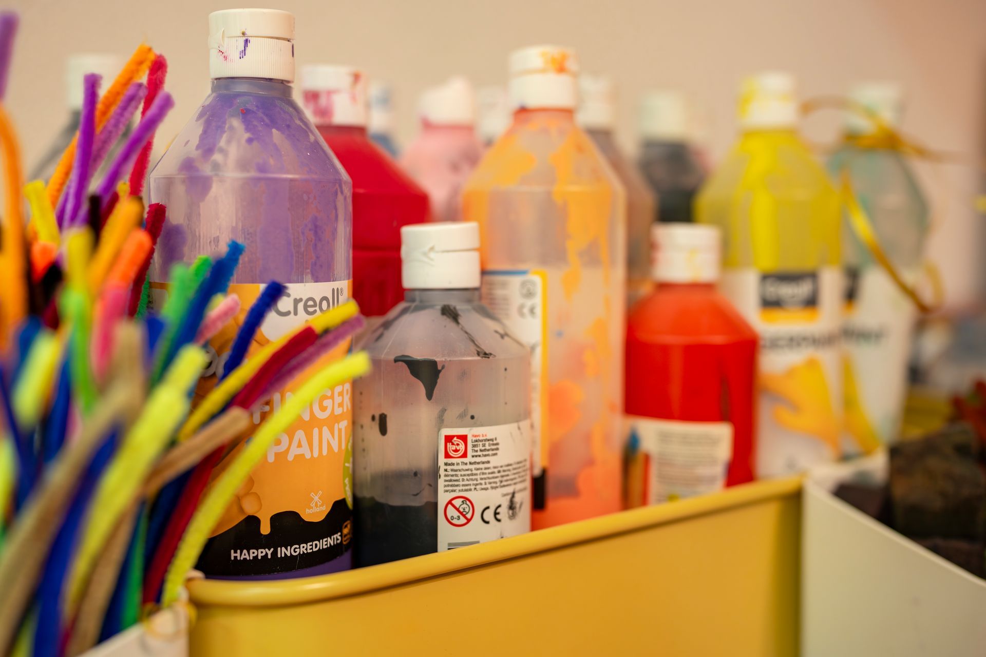 Kinder- und Erwachsenenhände klopfen in einem Innenraum auf eine hellbraune Holzkiste, vermutlich ein Schlaginstrument.