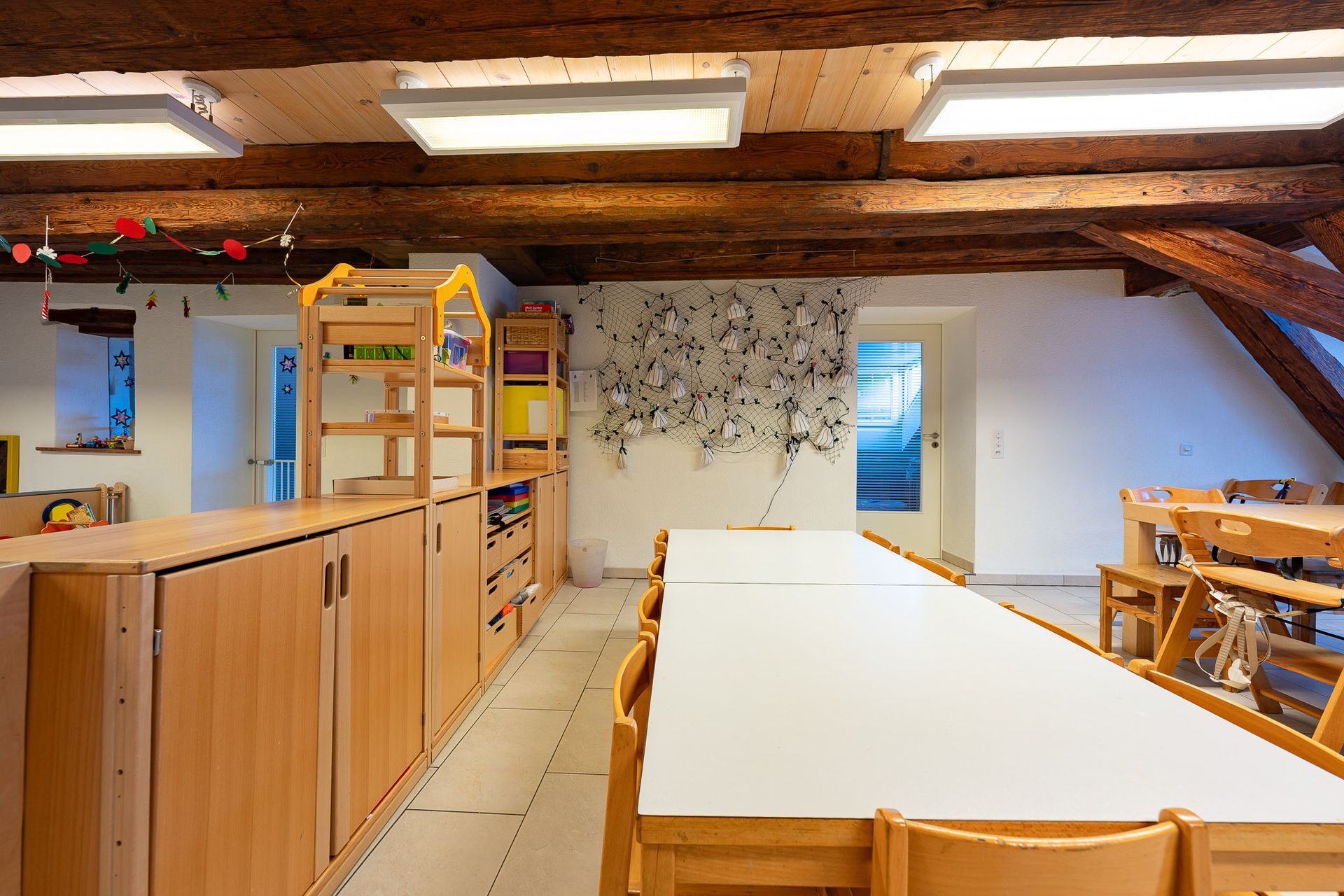 Schulraum aus Holz mit Tischen und Stühlen, Holzbalkendecke und Aufbewahrungsschränken.