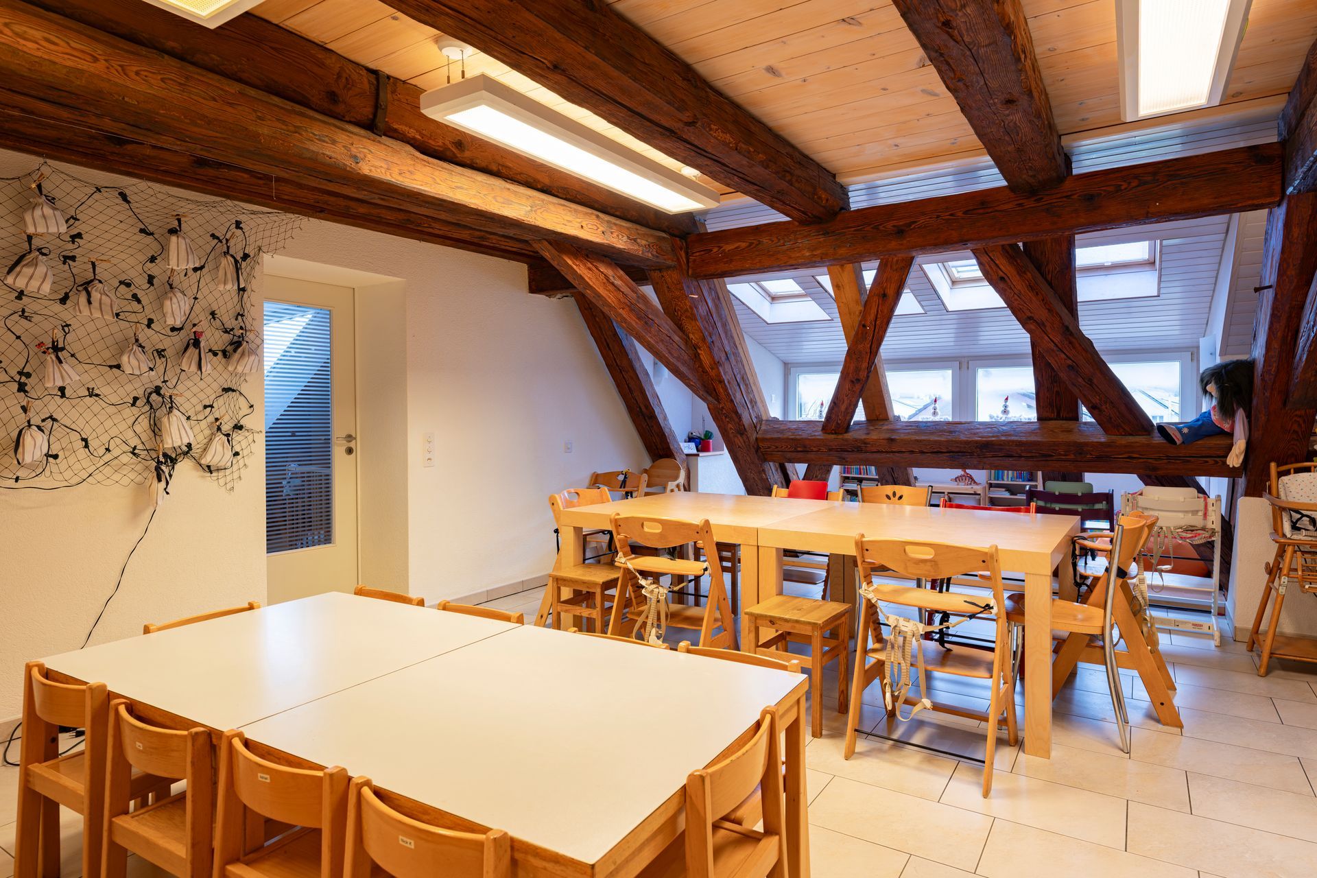 Kinder kleben weisse Papierausschnitte auf eine blaue Tischdecke mit Buntstiftzeichnungen.