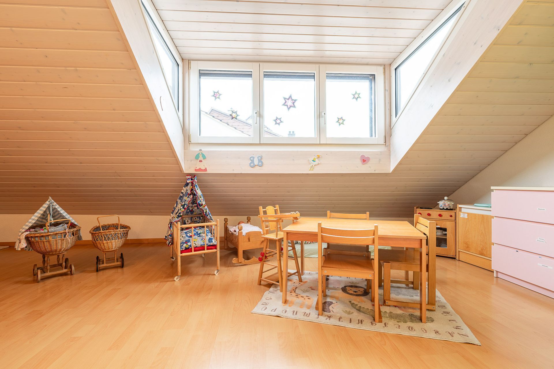 Spielzimmer mit Holzmöbeln, Dachschräge und großen Fenstern.