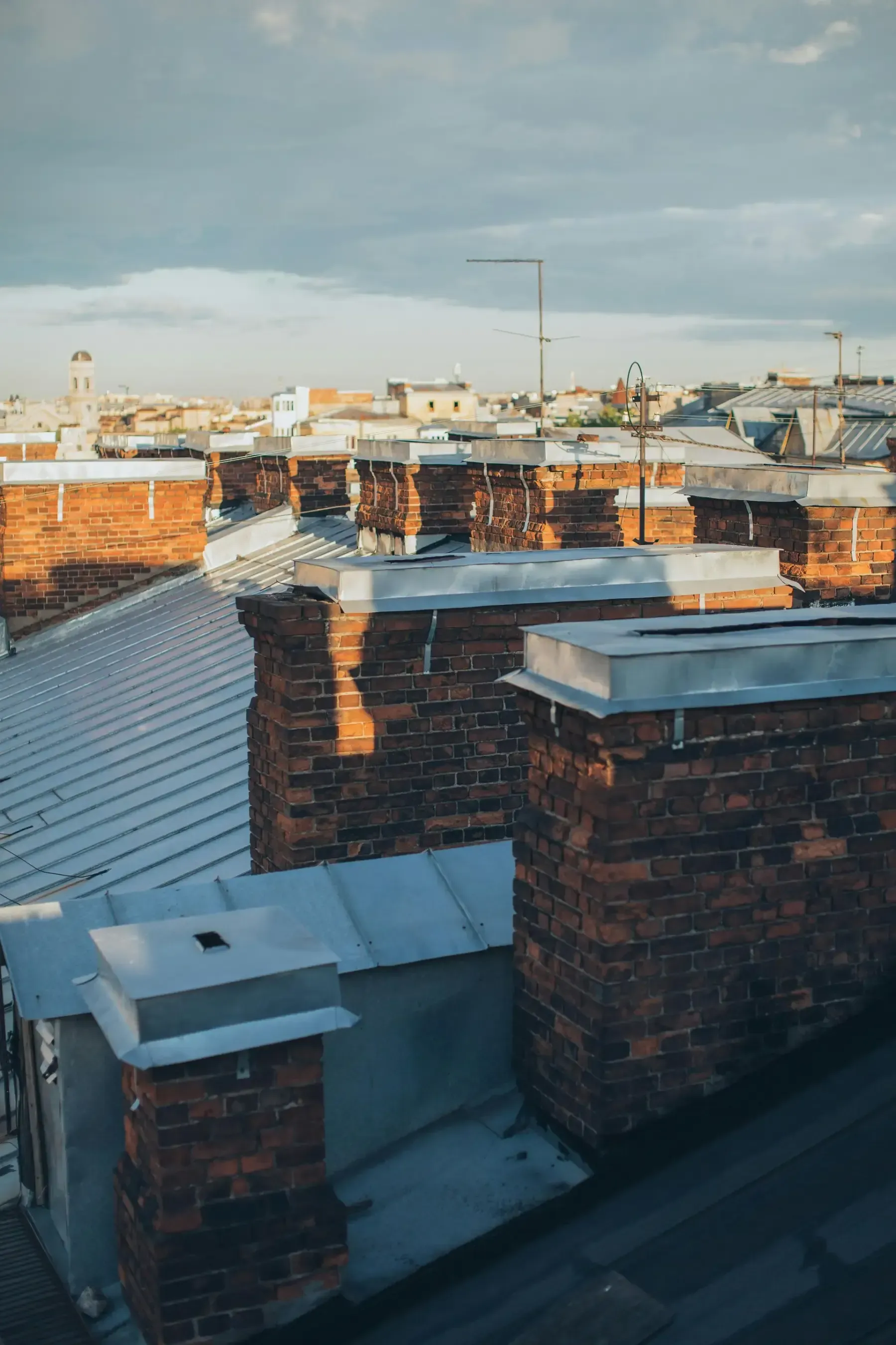 Chimeneas de ladrillo en los tejados, iluminadas por la luz del sol bajo un cielo nublado.