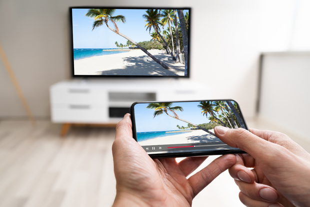 Una persona tiene in mano un cellulare davanti alla televisione