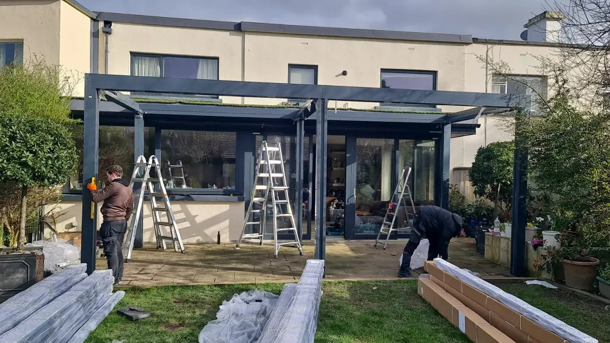 Eine Gruppe von Leuten arbeitet an einer Pergola vor einem Haus.