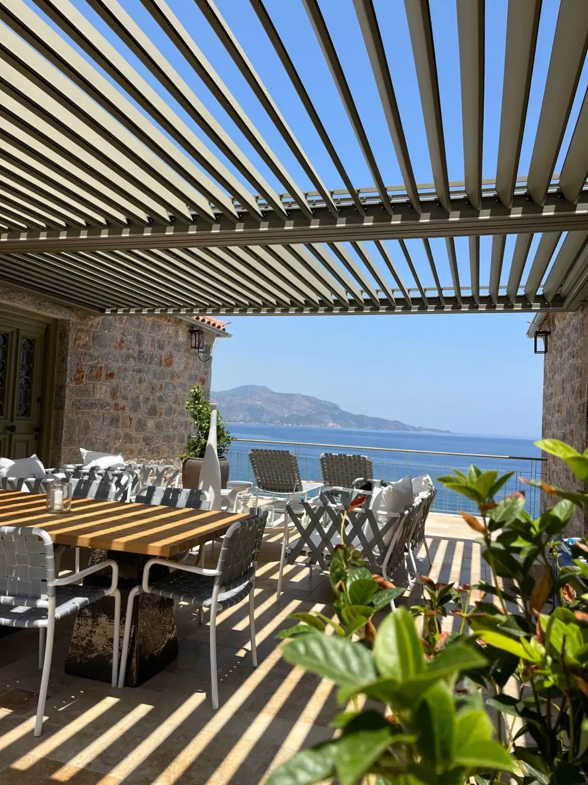 Eine Terrasse mit Tischen und Stühlen unter einer Pergola mit Blick auf das Meer.