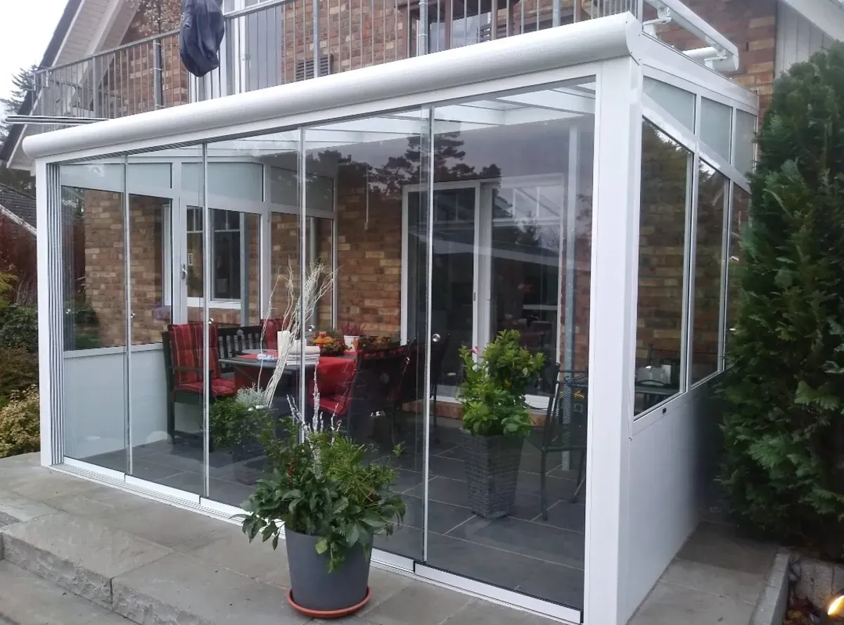 Ein weißer Wintergarten mit Glasschiebetüren und einer Topfpflanze davor.