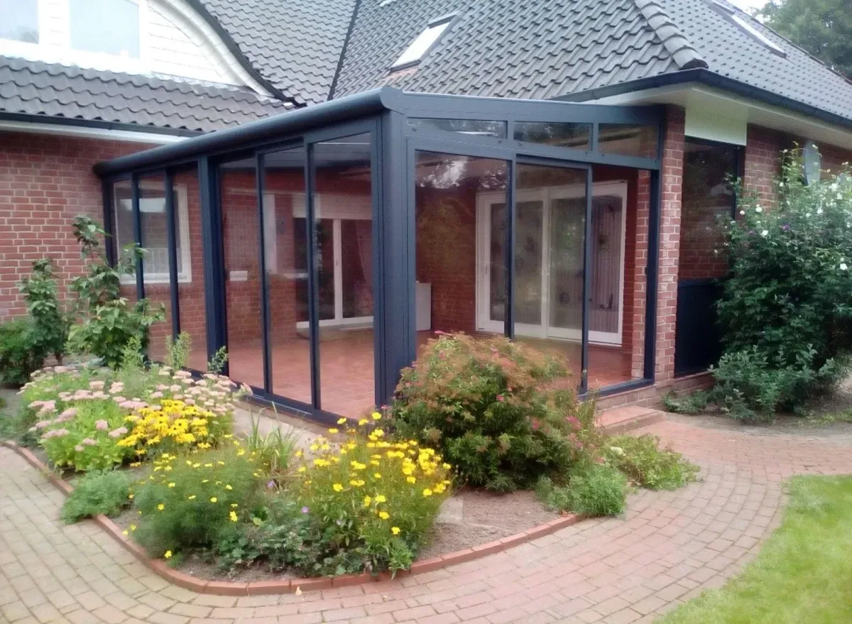 Ein Backsteinhaus mit einer glasüberdachten Veranda und einem Garten davor.