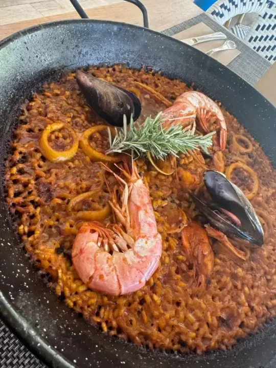 Paella de marisco en una sartén negra, cubierta con mejillones, gambas, rodajas de limón y romero.