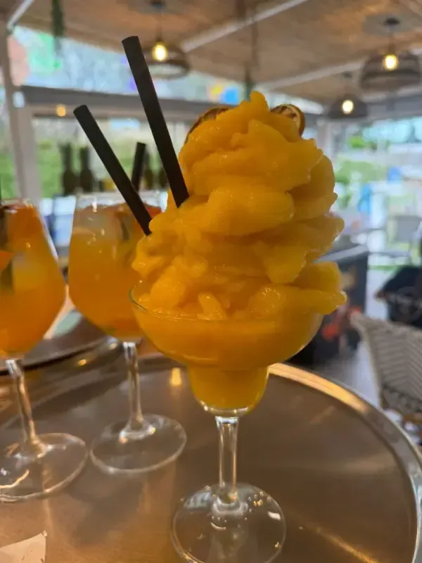 Sorbete de mango amarillo en una copa con tallo sobre una bandeja, con dos copas de vino y pajitas.