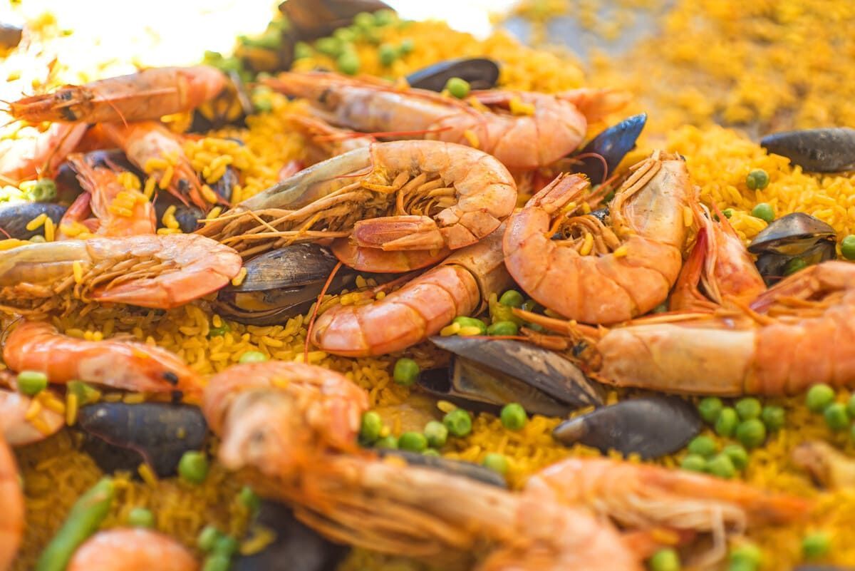 Paella de marisco en una sartén negra con mejillones, gambas, rodajas de limón y guarnición de romero.