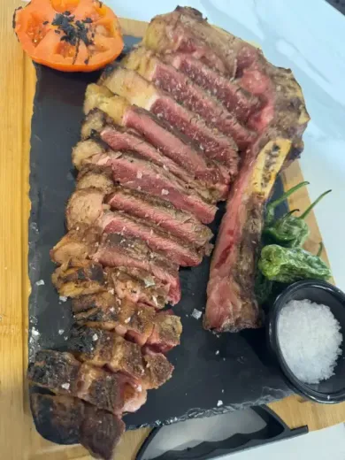 Filete en rodajas emplatado con verduras asadas, medio tomate y sal en una tabla de servir de pizarra negra.