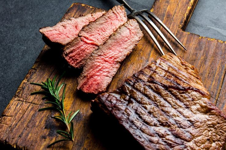 Filete en rodajas sobre una pizarra negra con verduras a la parrilla y sal gruesa sobre una mesa de madera.