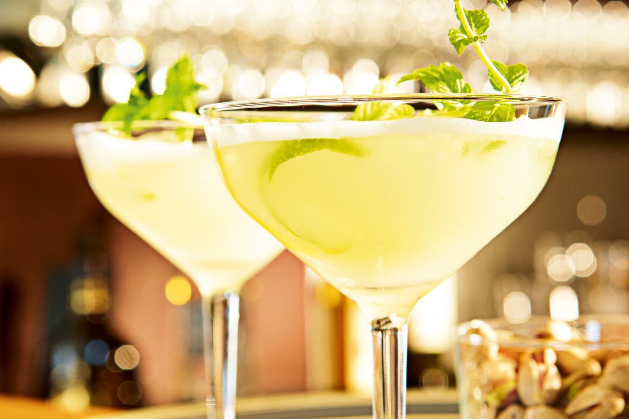 Dos copas de martini heladas con rodaja de limón y menta sobre una barra tenuemente iluminada.