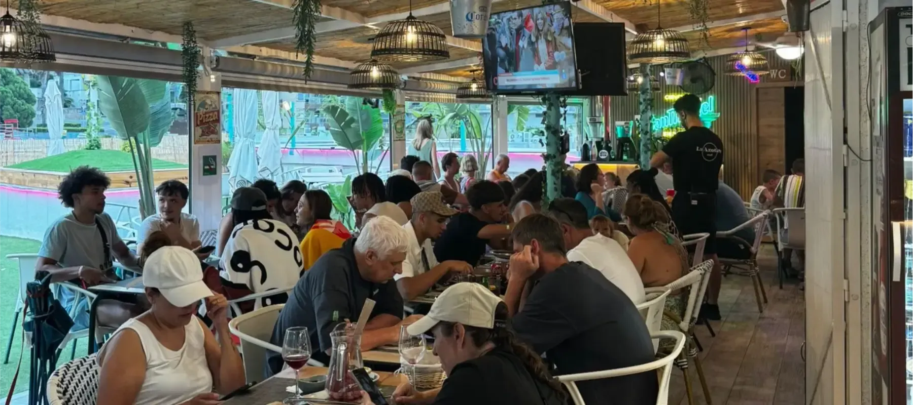 Cafetería al aire libre abarrotada de gente comiendo y charlando bajo un patio cubierto.