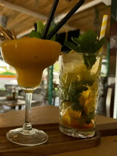 Dos cócteles tropicales en una bandeja de madera, uno en una copa margarita y otro en un vaso alto con menta