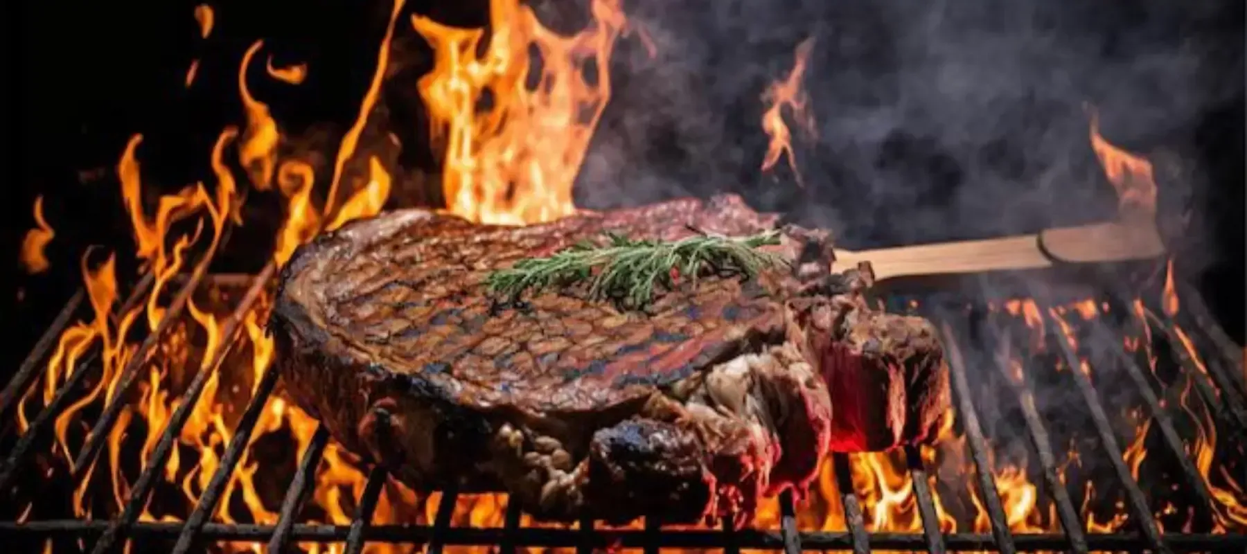 Un filete chisporroteando en la parrilla sobre llamas abiertas, con humo y brasas incandescentes.