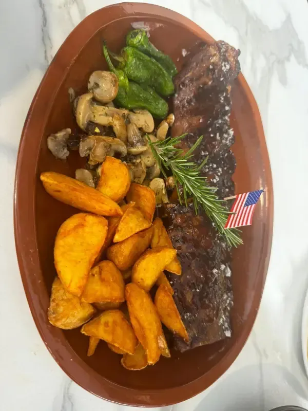 Cena de bistec con papas fritas, verduras salteadas, romero y una pequeña bandera estadounidense en un plato ovalado.