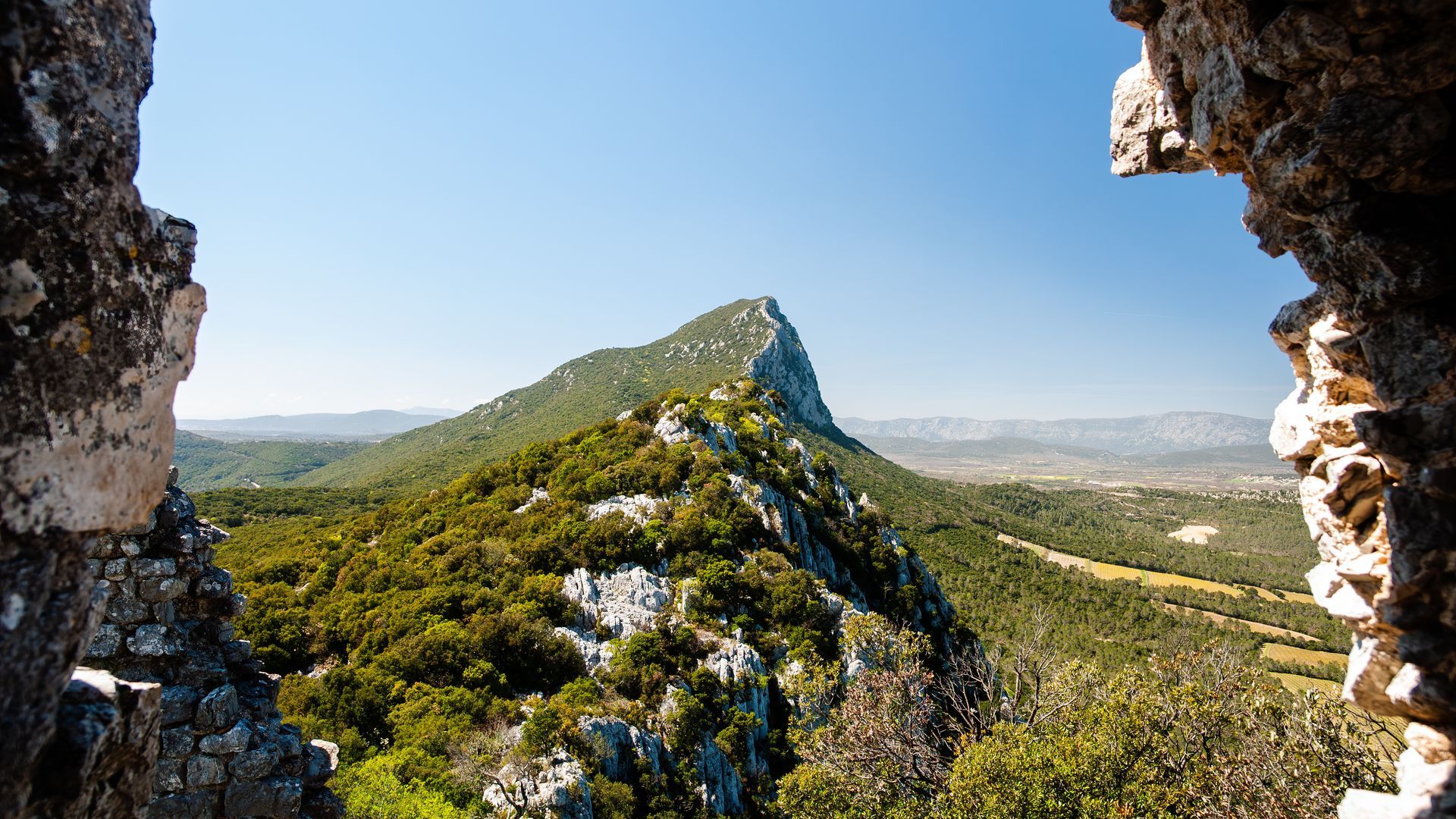 Crête montagneuse aperçue à travers une ouverture dans la pierre, avec un ciel bleu clair et un paysage verdoyant luxuriant.