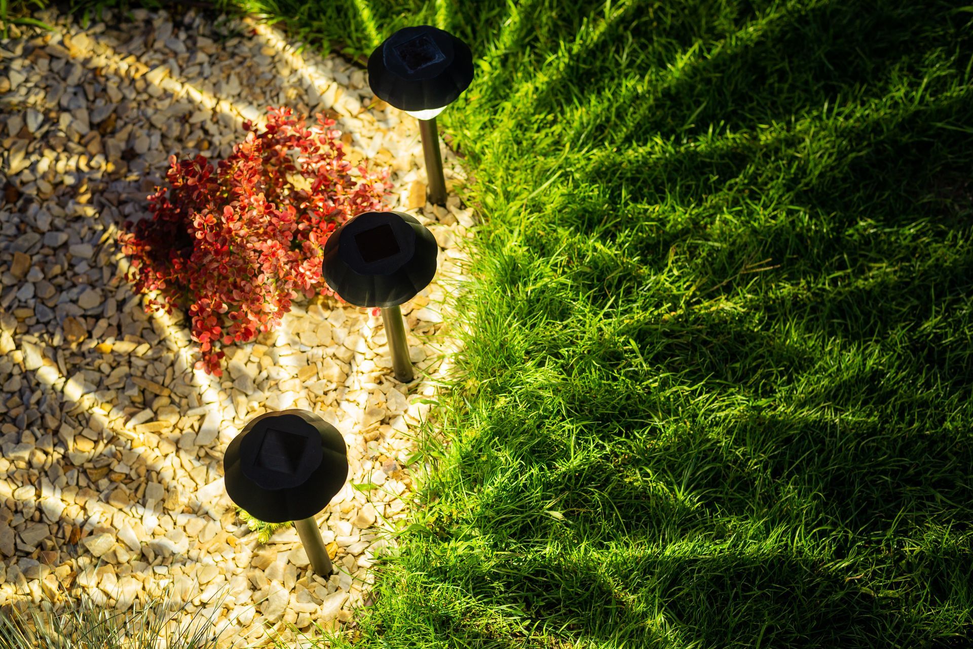 Les lampes solaires de jardin illuminent la pelouse et le gravier, projetant des ombres aux motifs géométriques.
