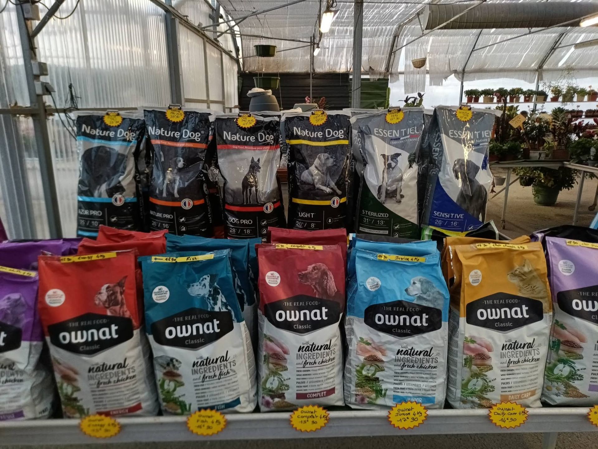 Des sacs de nourriture pour chiens présentés sur une étagère dans un magasin, portant les marques Ownat et Advance.