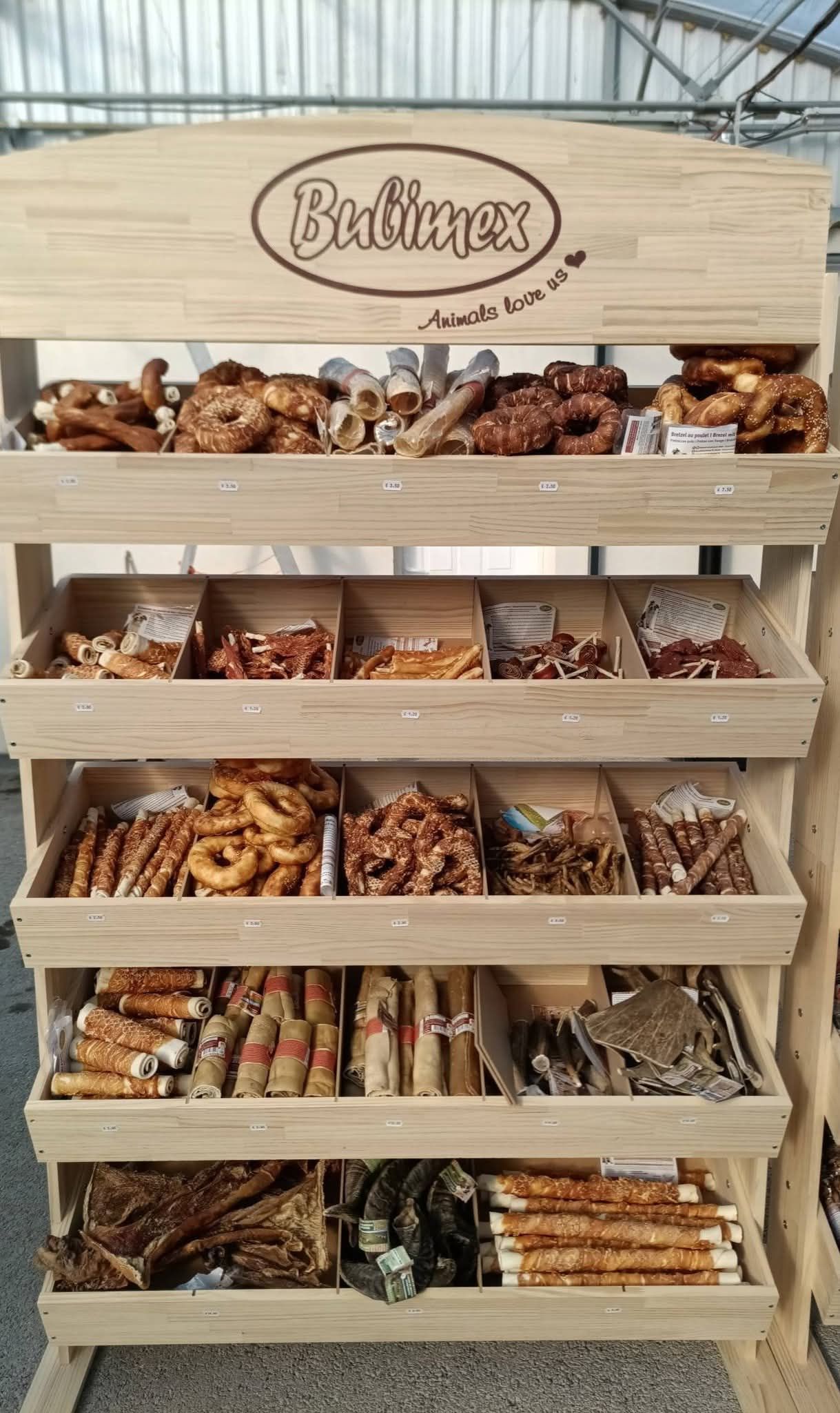 Présentoir en bois contenant diverses friandises pour chiens. Le présentoir comporte plusieurs étagères présentant différents types de friandises.