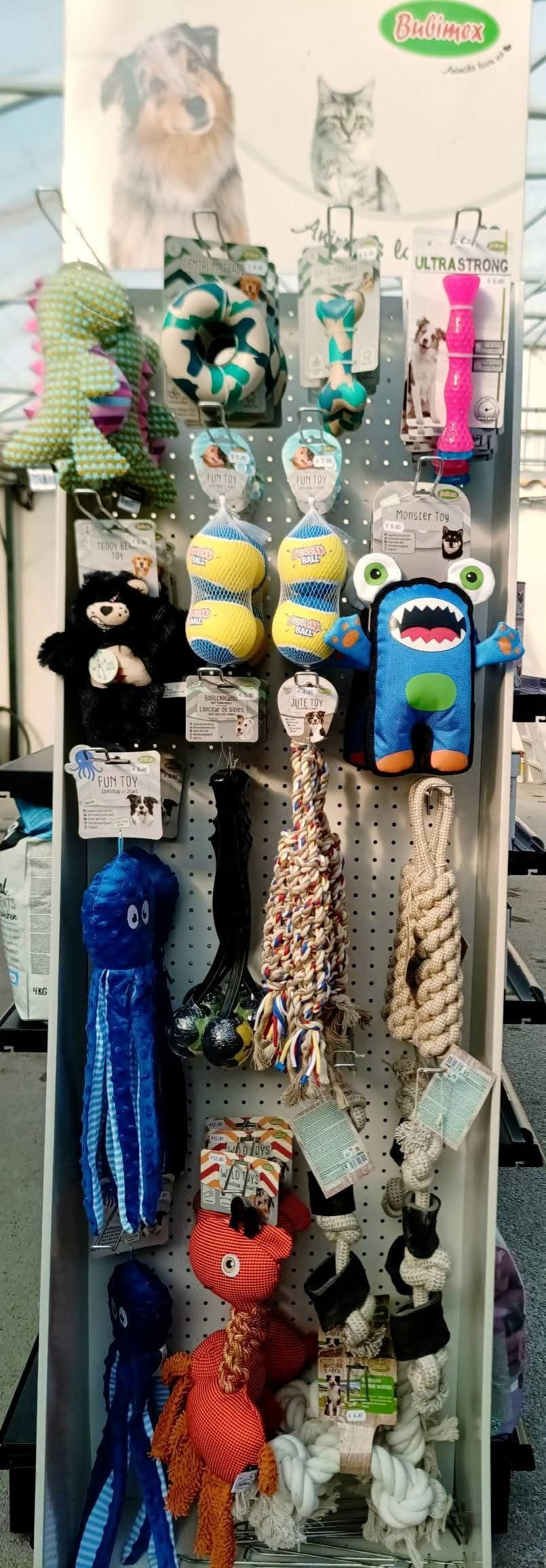 Présentoir de jouets pour chiens comprenant divers jouets en peluche et cordes, dans un environnement de magasin.