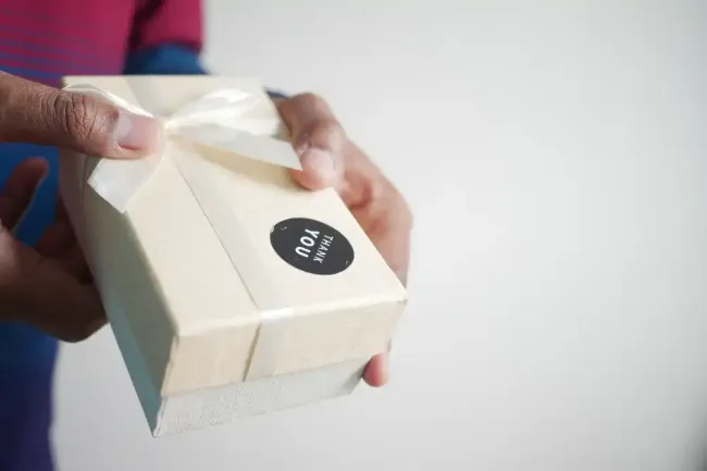 A person is holding a white box with a bow on it.