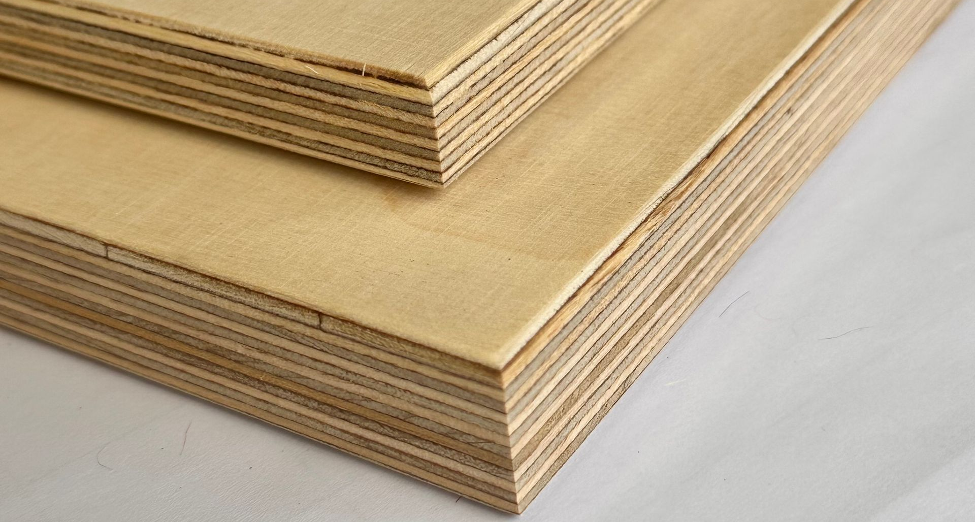 Nahaufnahme von zwei Stapeln hellfarbiger Sperrholzplatten, die den geschichteten Aufbau des Materials zeigt.