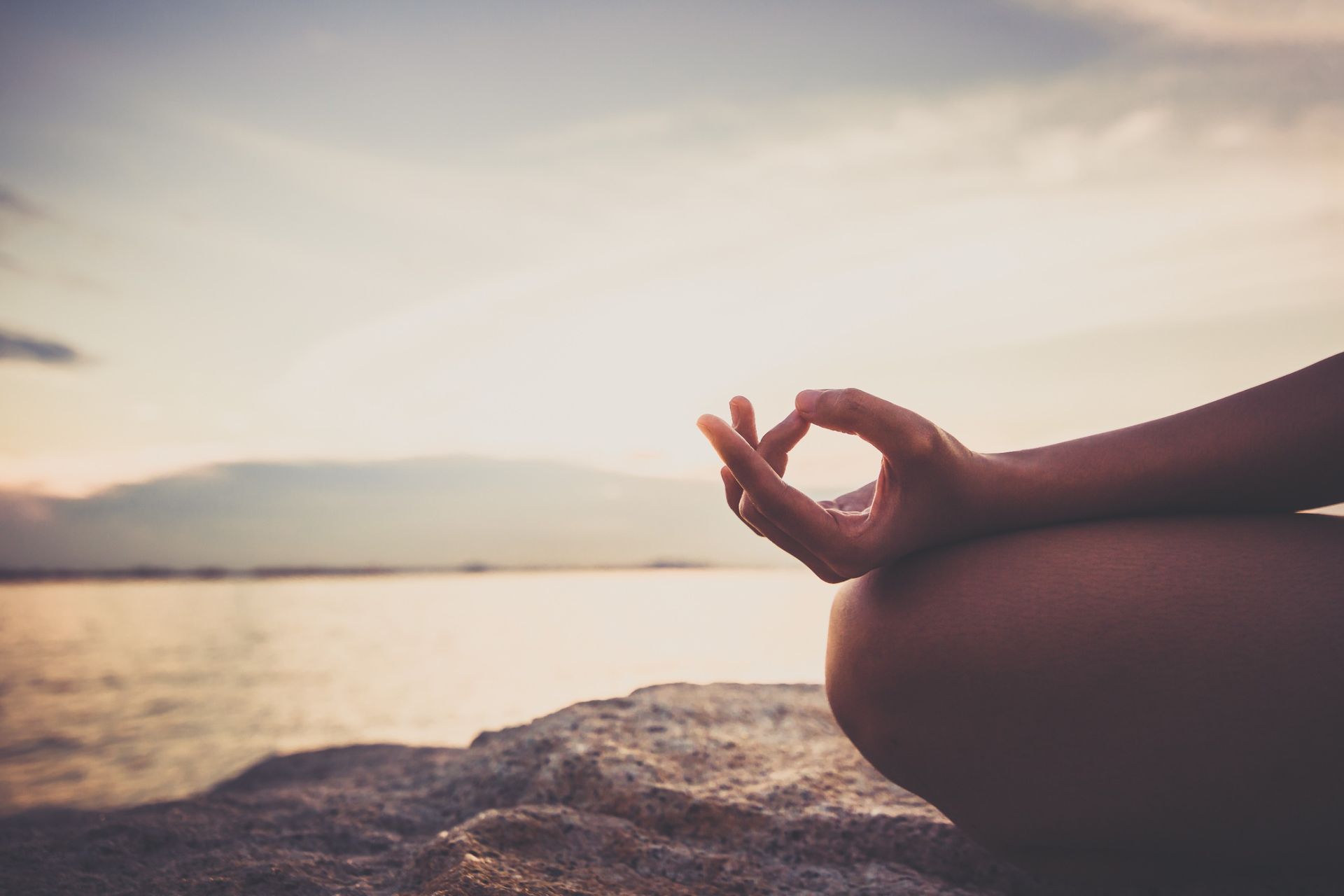 Una persona está meditando en una roca cerca del agua.