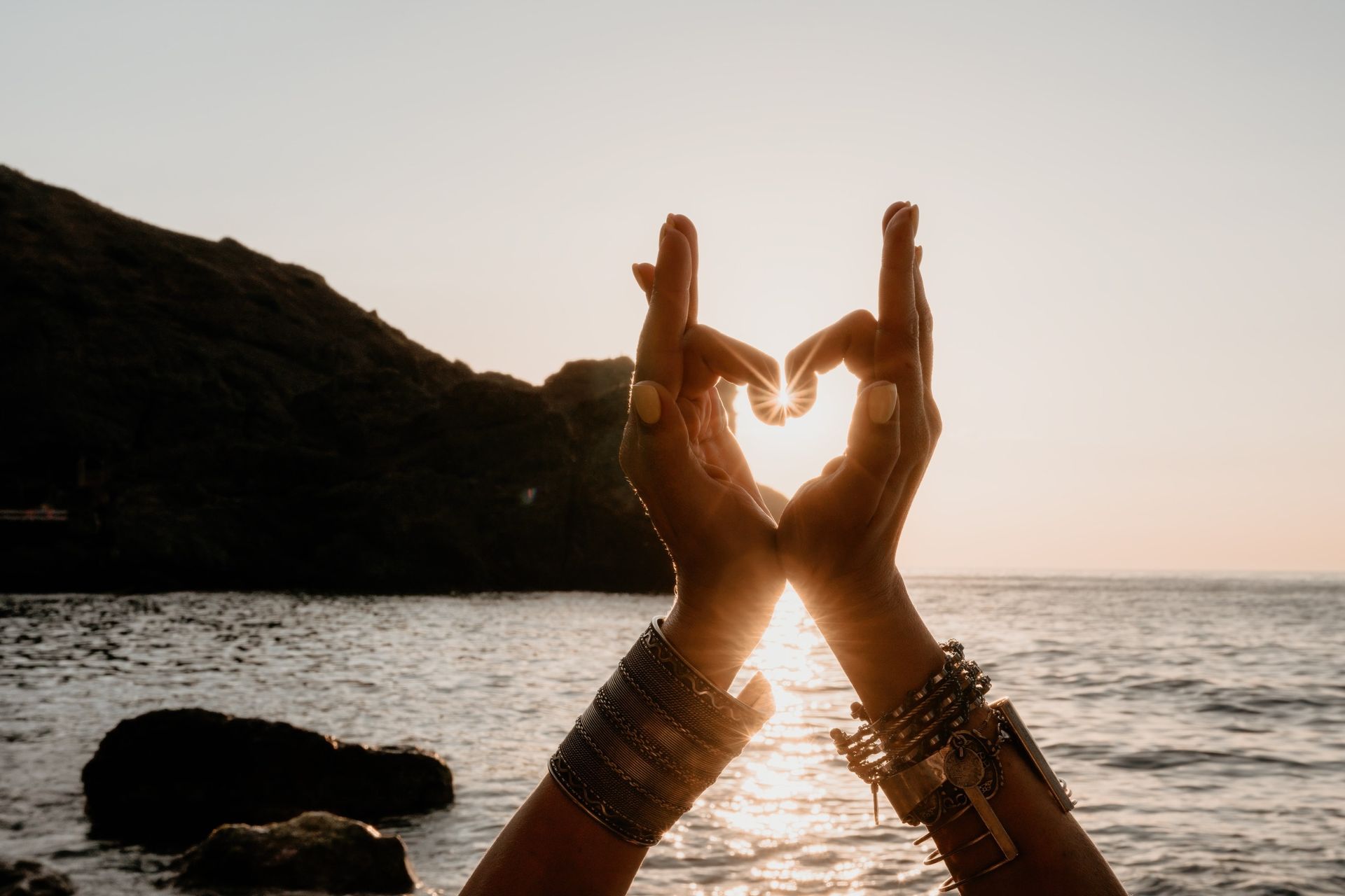 Una mujer está haciendo una forma de corazón con sus manos en la playa.