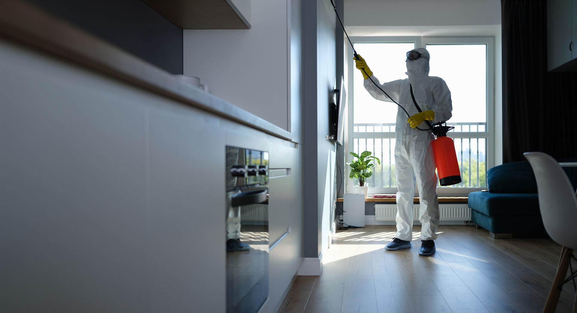 Une personne en combinaison de protection pulvérise de l'insecticide dans un appartement moderne.