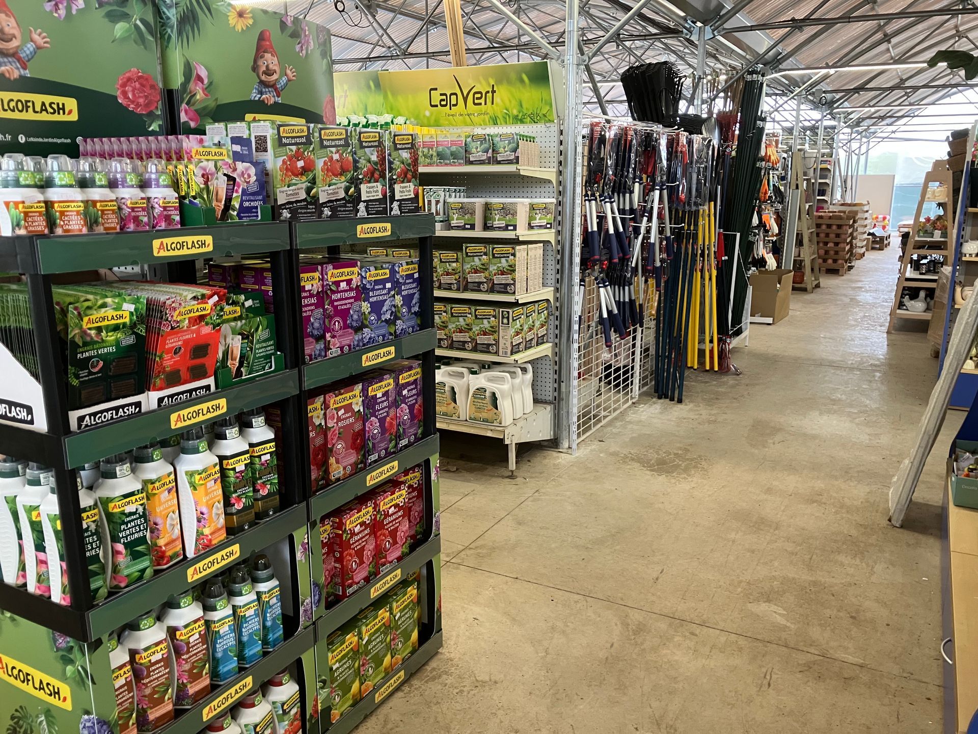 Une allée d'un magasin de jardinage présentant des étagères remplies de divers produits d'entretien des plantes et d'outils de jardin suspendus.