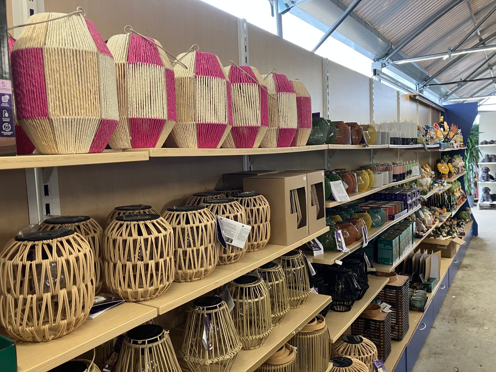 Dans un magasin, des étagères présentent des paniers tressés et des lanternes aux tons naturels beige et rose, ainsi que divers articles de décoration intérieure.
