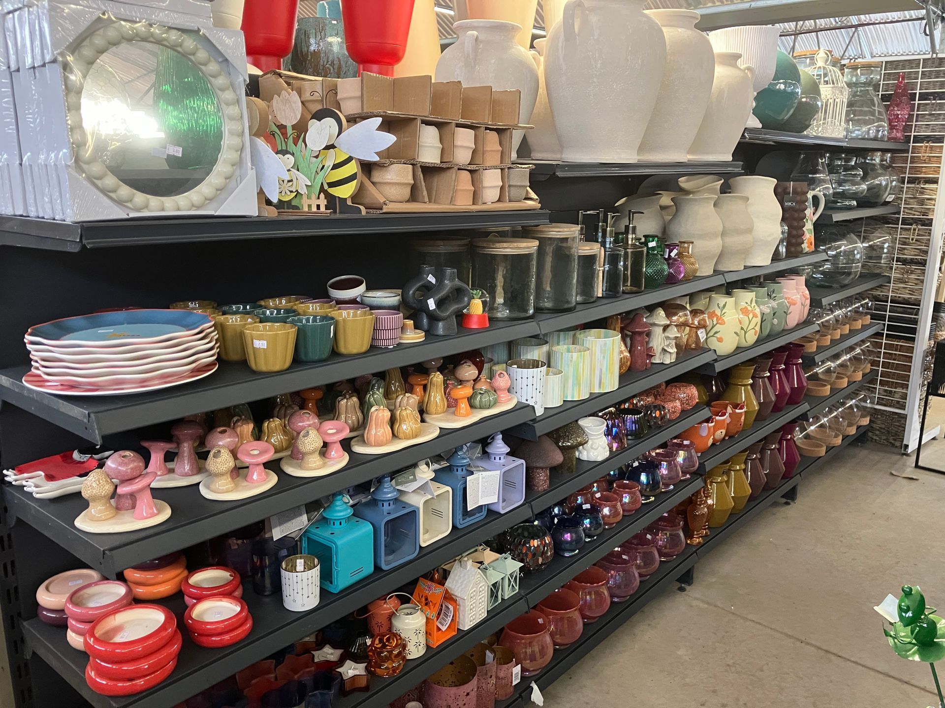 Les rayons d'un magasin regorgent d'articles de décoration variés, notamment des vases blancs, des bols colorés et des petites figurines.