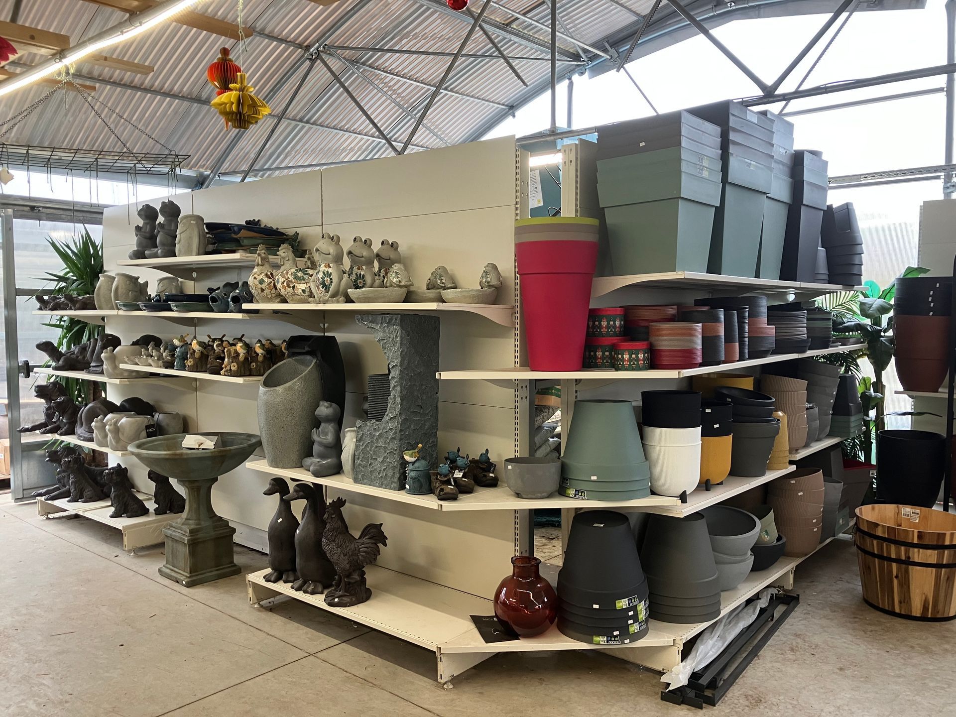 Une étagère de magasin dans une serre présentant divers pots de jardin, des bains d'oiseaux et des figurines décoratives.