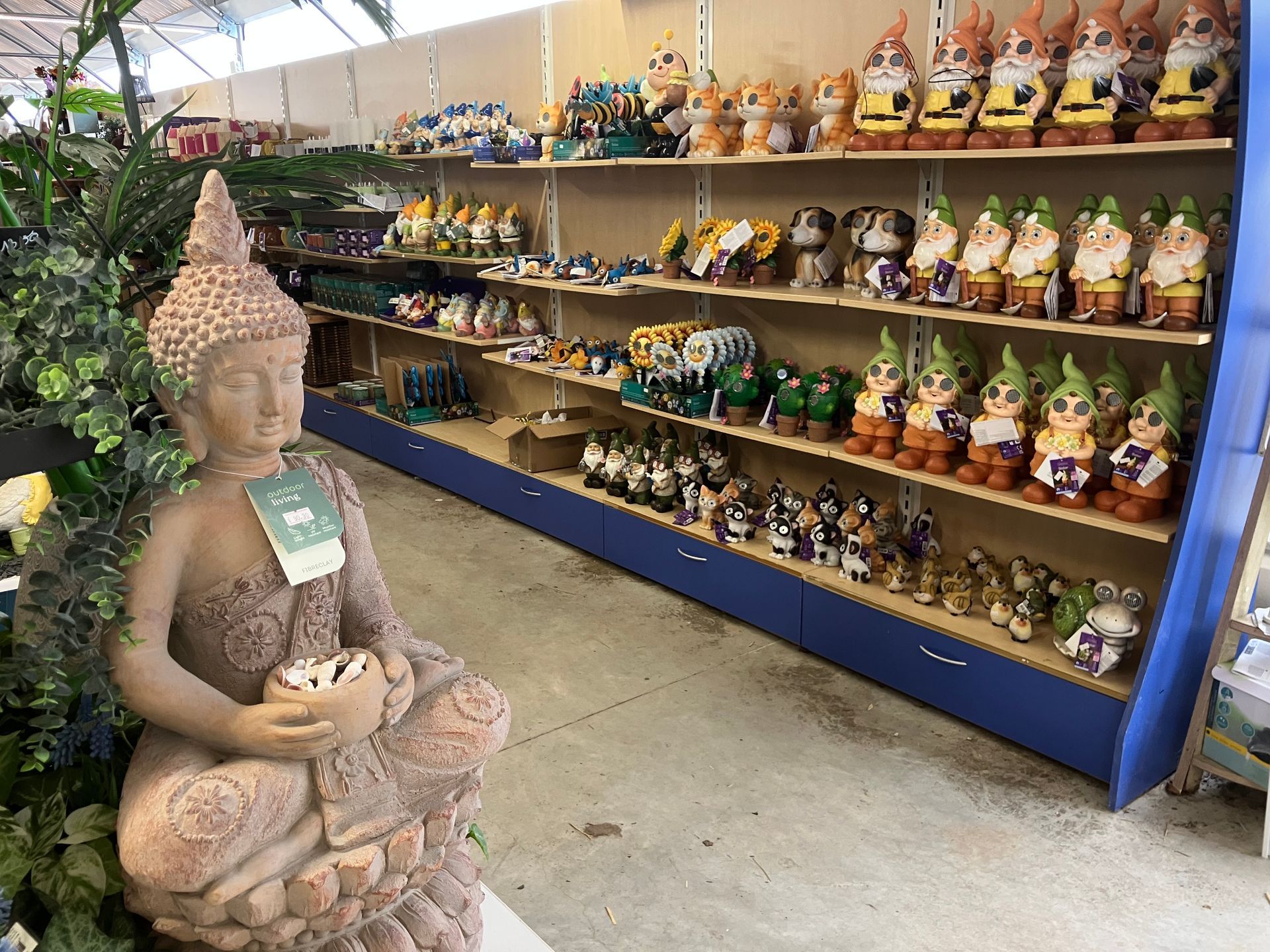 Au premier plan, une statue de Bouddha en pierre fait face à une étagère remplie de nains de jardin et d'ornements dans un magasin.