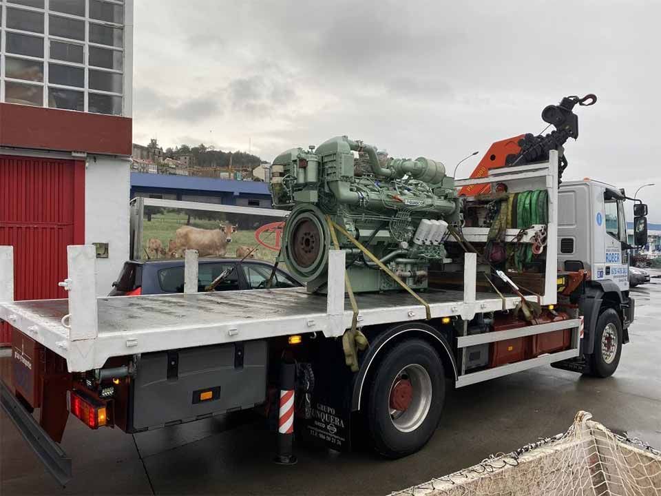 Un camión de plataforma con una grúa en la parte trasera transporta un motor grande.