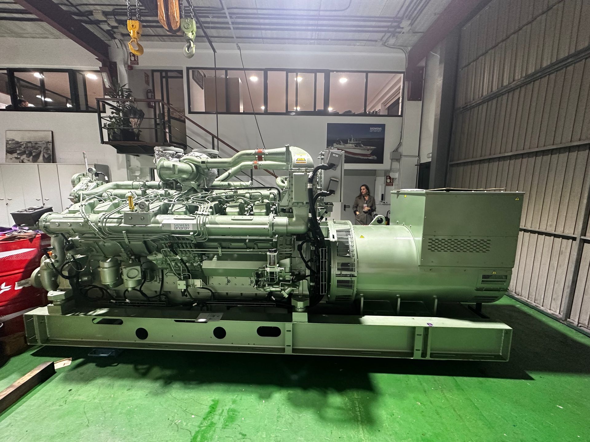 Un motor grande está estacionado en un almacén al lado de un automóvil rojo.