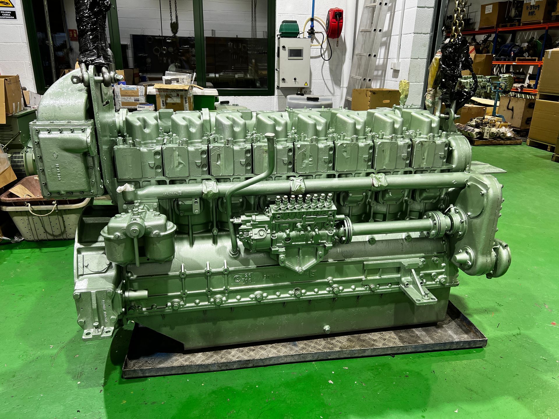 Un gran motor está estacionado sobre una alfombra verde en un almacén.