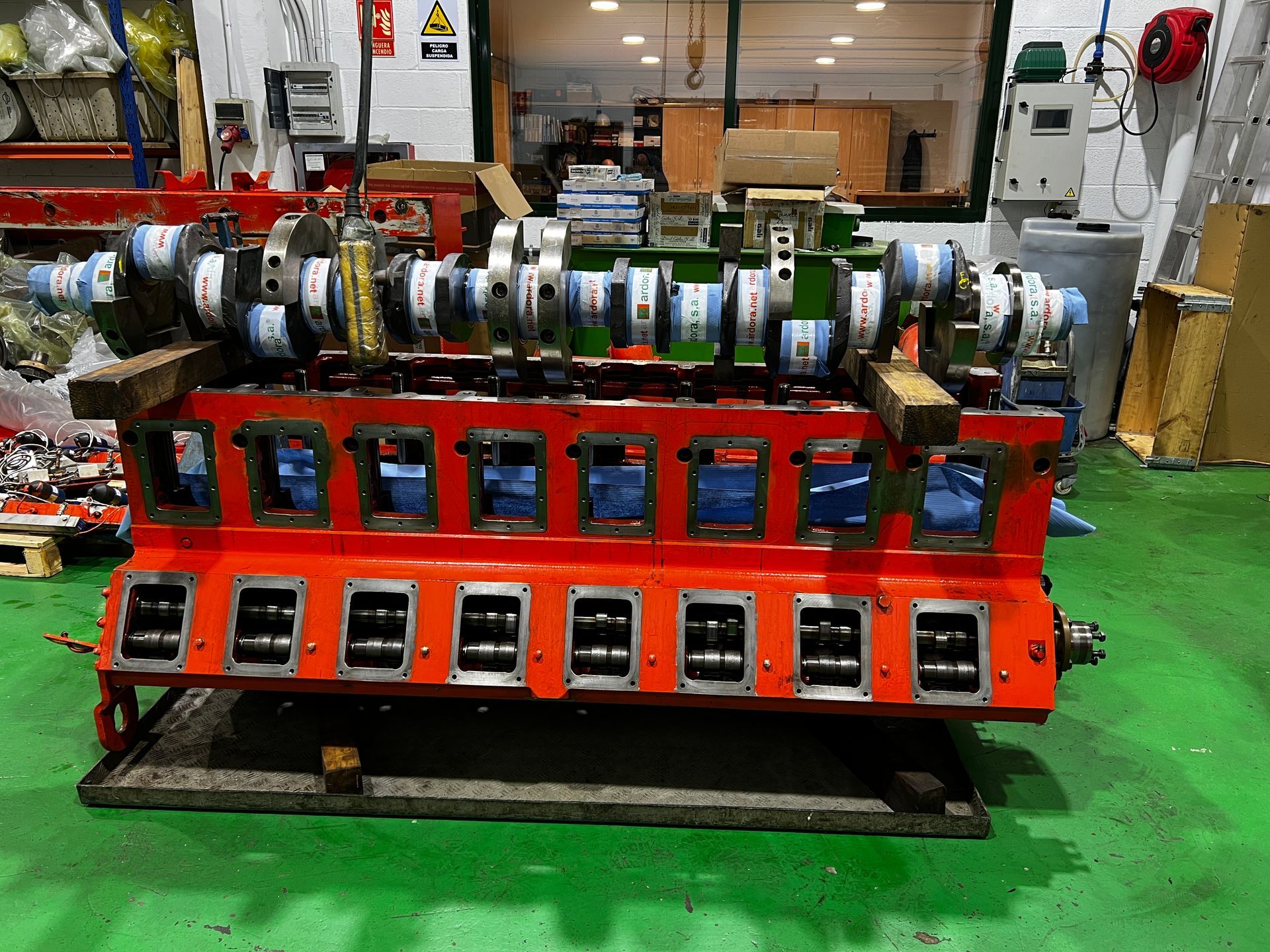Una gran máquina roja está colocada sobre un suelo verde en una fábrica.