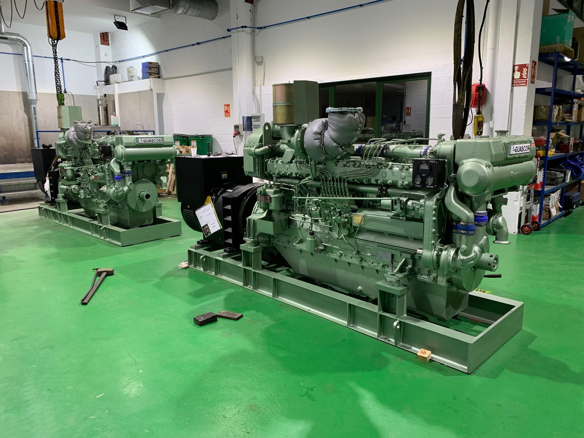 Dos motores están estacionados sobre un suelo verde en un almacén.