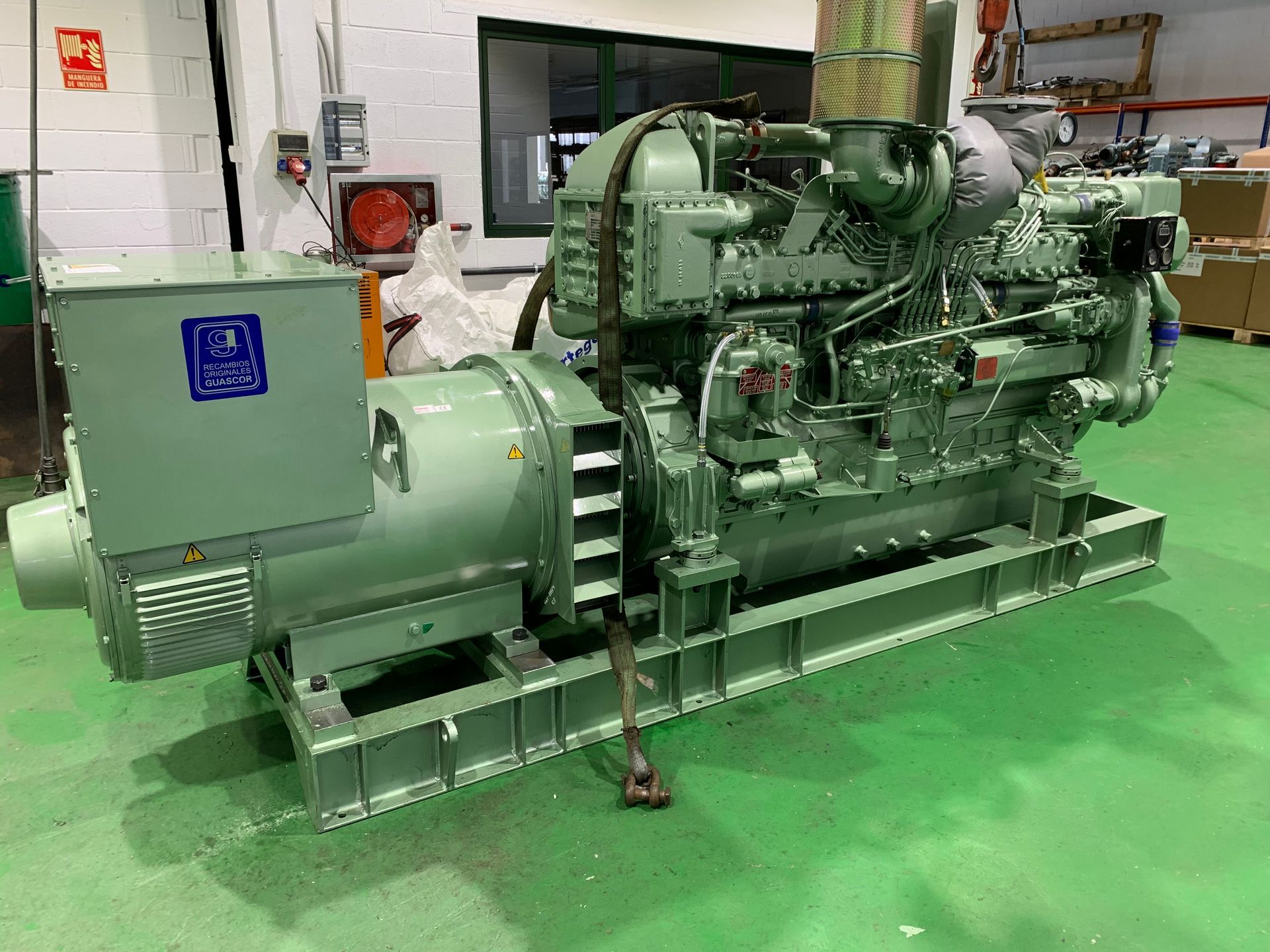 Un gran generador diésel se encuentra sobre un suelo verde en un almacén.