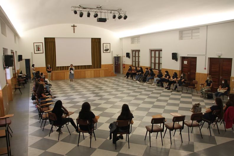 Auditório com pessoas sentadas em círculo de frente para um palco e um telão.