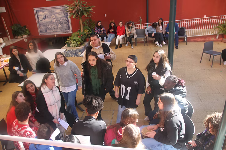 Um grupo de pessoas estava reunido em um pátio de paredes vermelhas, conversando em pé perto de bancos e mesas.