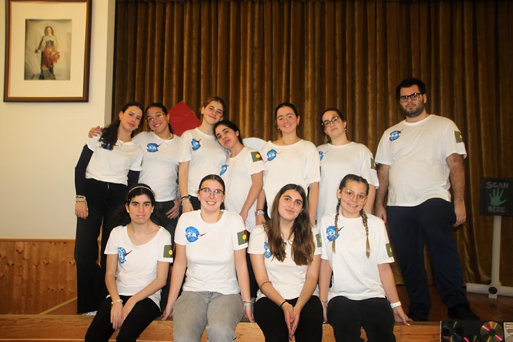 Grupo de pessoas vestindo camisas brancas posando juntas em um palco com cortinas marrons.