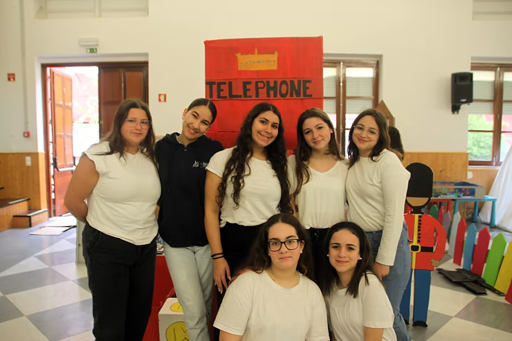 Seis pessoas posando em um ambiente interno em frente a uma cabine telefônica vermelha.