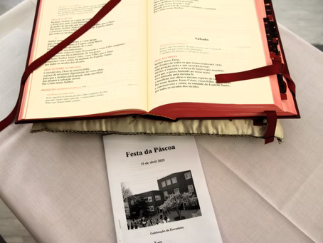 Livro vermelho aberto com fitas vermelhas sobre um pano branco, ao lado de um programa intitulado “Festa da Pessoa”.